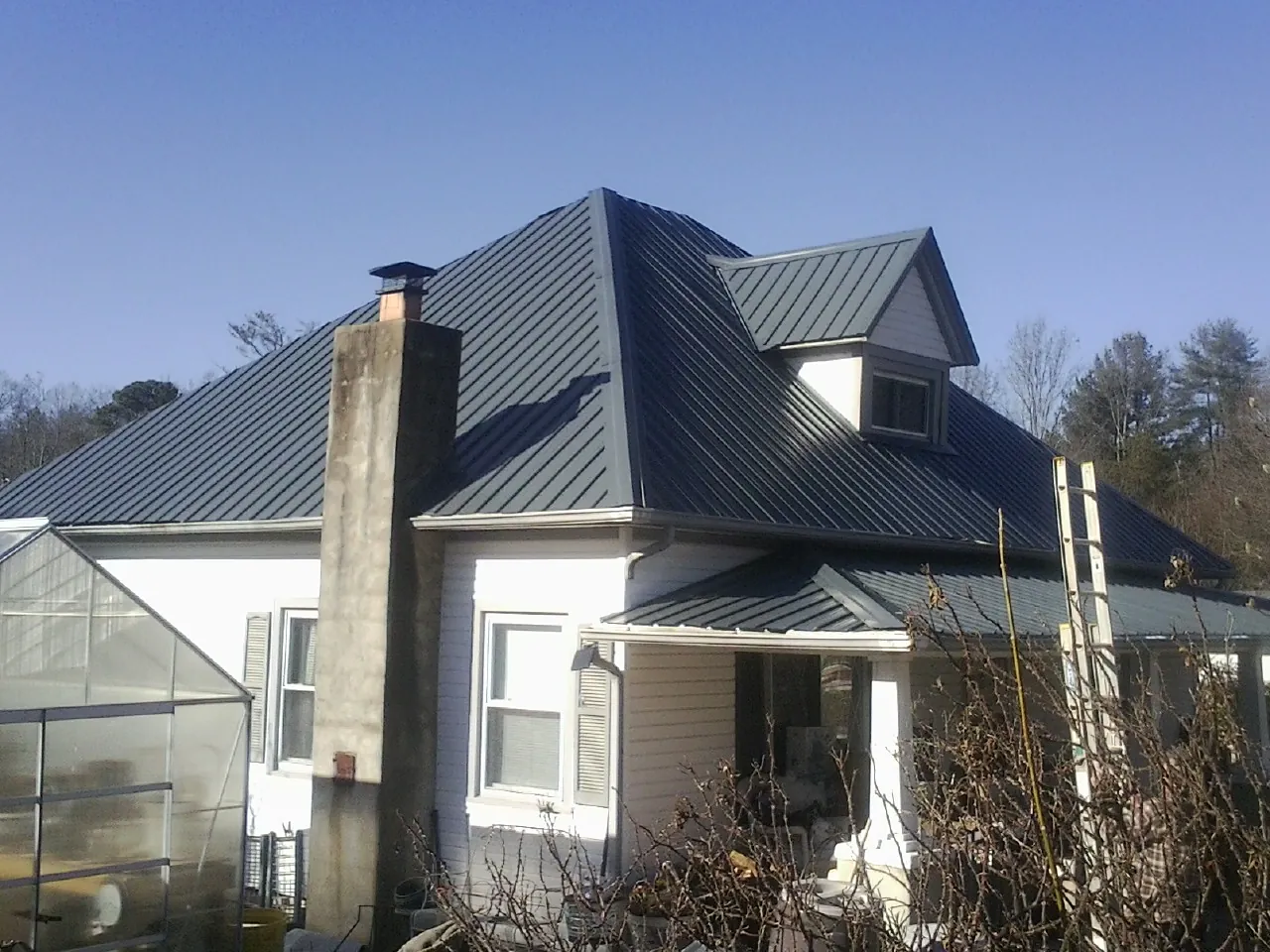 Dark blue standing seam metal roof on a white farmhouse with dormer — Slate & Tile Roof Repair by Roofing Brothers in Cedaredge