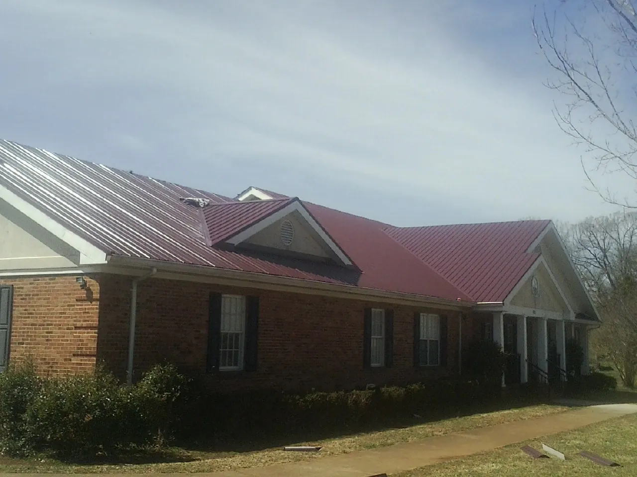 Red metal roof with gabled entries on a long brick building, from a Hail Damage Roof Repair job in Cedaredge