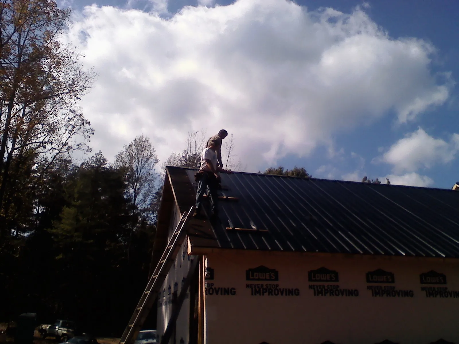 Roofer fastening dark metal panels high against a cloudy sky, from a Roof Inspection job in Cedaredge
