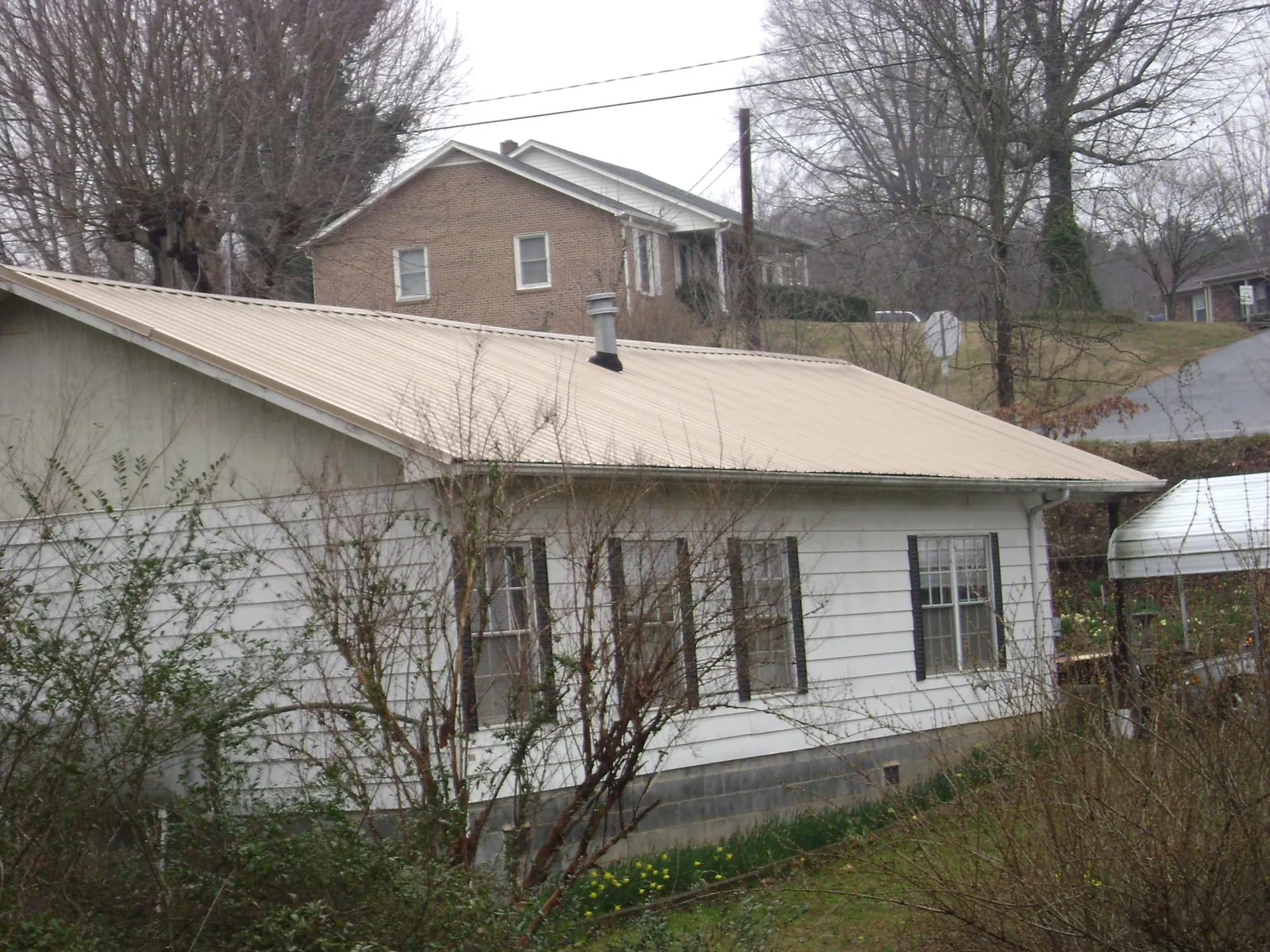 Tan metal roof on a white sided house set into a hillside — Commercial Roofing by Roofing Brothers in Cedaredge